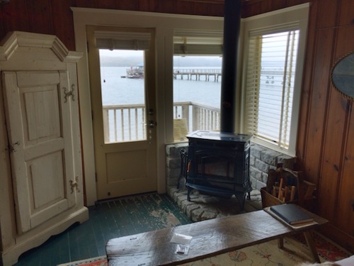 The living room of Al's, with a view of the boat shack past the porch. Please note the wood stove, ready for lighting — a source of much coziness later in the evening.