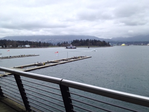 Looking north towards Stanley Park — a seaplane is accelerating towards takeoff over Coal Harbor.